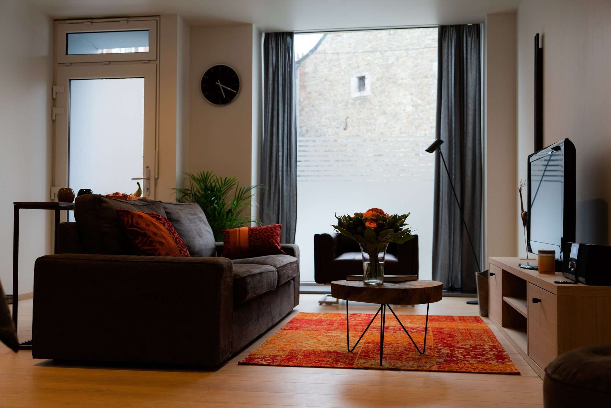 Coin salon devant la grande baie vitrée, canapé, table basse en bois et bouquet de fleurs