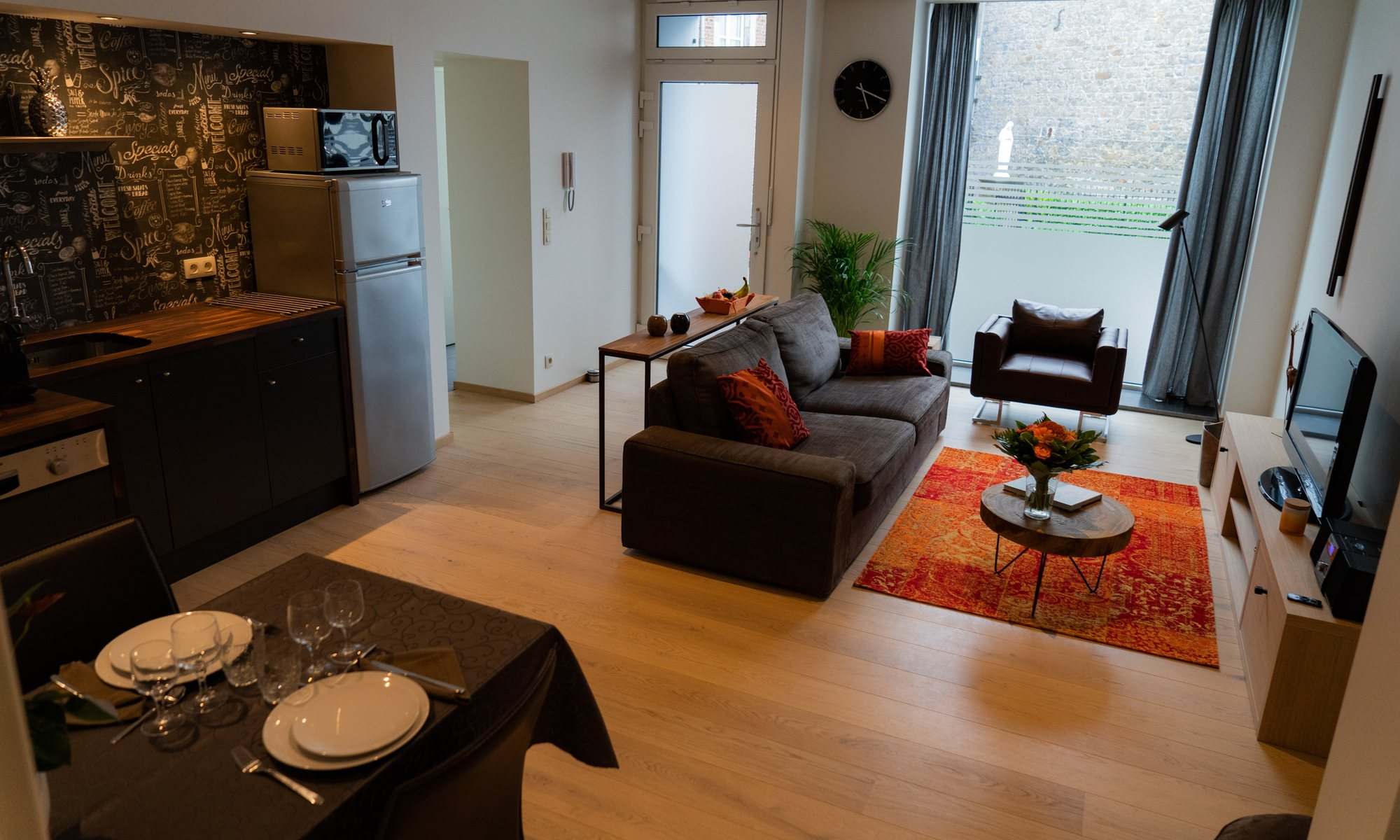 Le séjour de l'appartement : coin cuisine, table dressée pour deux et salon au tapis orange